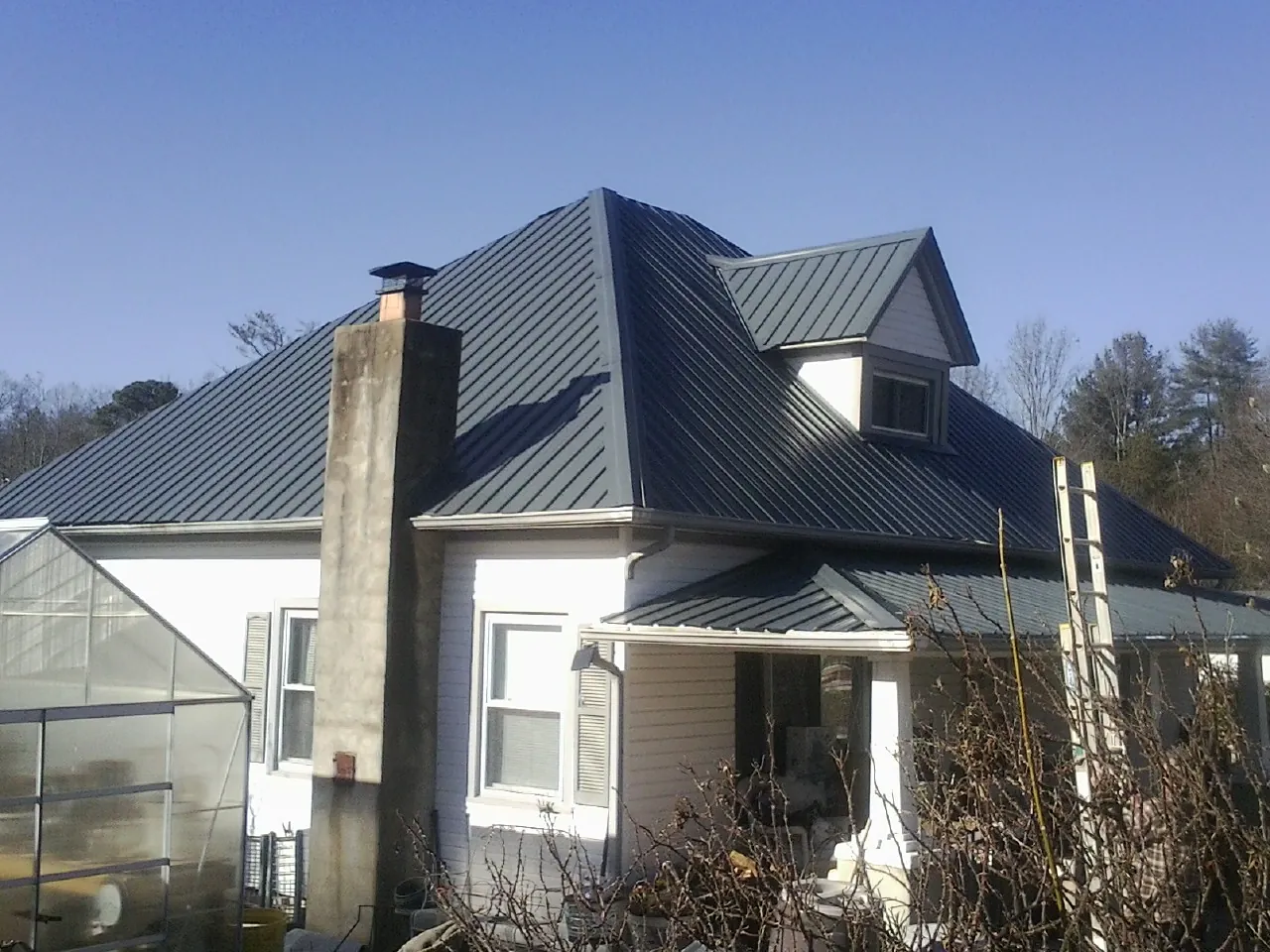 Dark blue standing seam metal roof on a white farmhouse with dormer — Slate & Tile Roof Repair by Roofing Brothers in Lake Orion