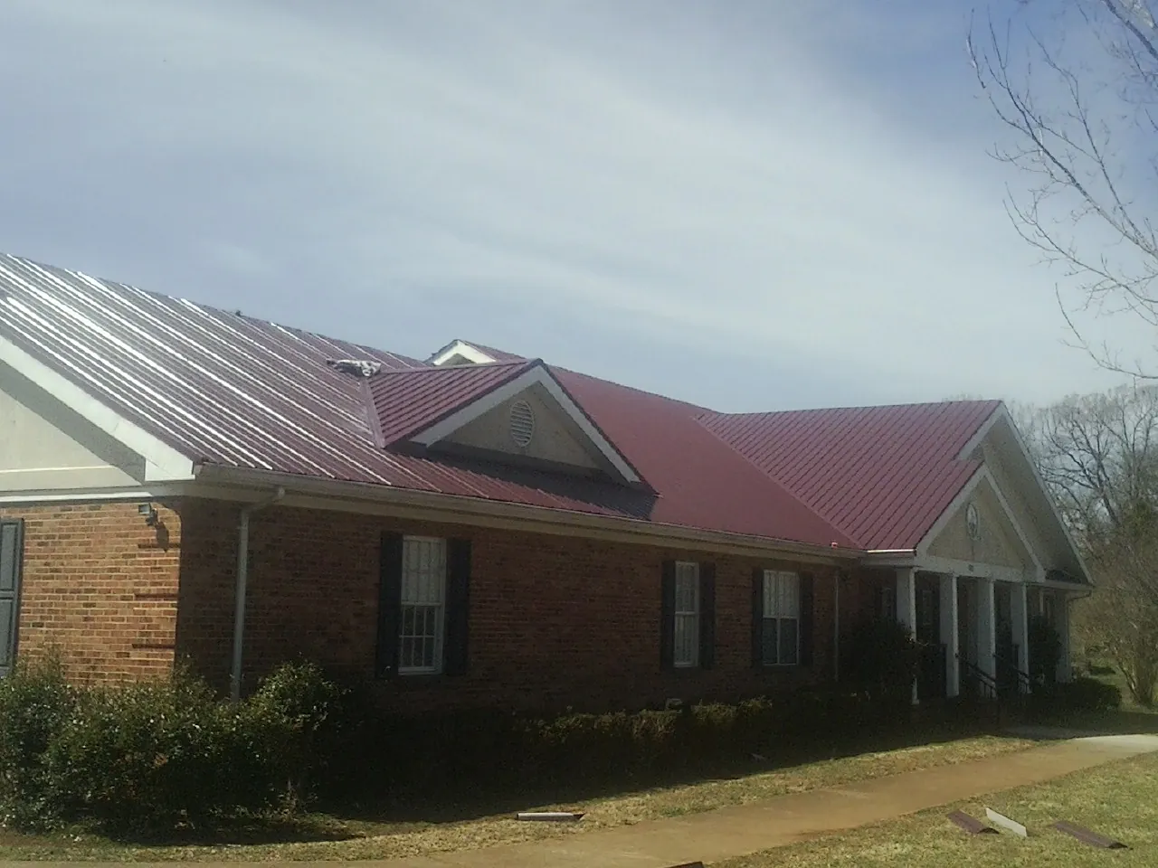 Red metal roof with gabled entries on a long brick building, from a Hail Damage Roof Repair job in Lake Orion