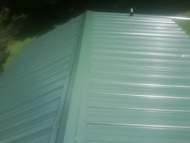 New green metal panels meeting at the ridge of a roof — Flat Roof Repair work by our crew in Lake Orion