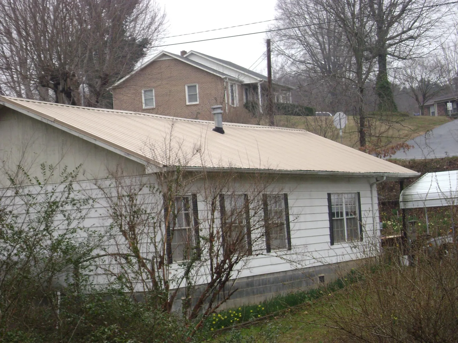Tan metal roof on a white sided house set into a hillside — Commercial Roofing by Roofing Brothers in Lake Orion